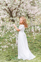 Obraz na płótnie Canvas Beautiful young girl in a white long dress in a blooming spring garden