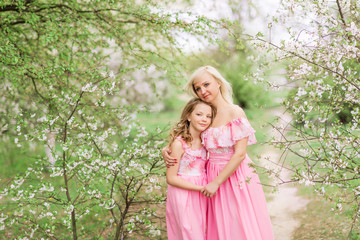 Fototapeta na wymiar Mother and daughter in pink dresses in a blooming garden in spring.