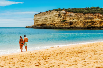 Young couple enjoying beautiful, sandy beach with cliffs in Algarve, Portugal