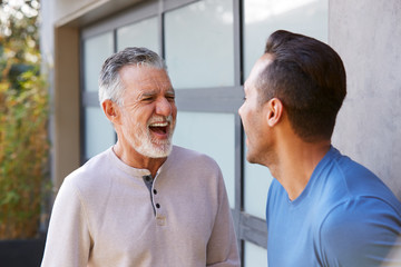 Senior Hispanic Man Talking And Laughing With Adult Son In Garden At Home - obrazy, fototapety, plakaty