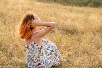 Tender beautiful red-haired girl enjoys the sunset in a field with a hill.
