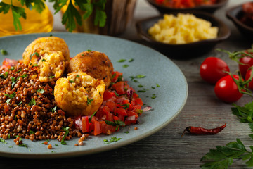 Lentil and millet meatballs. Served on tomato salsa with buckwheat. Gray plate, wooden boards in the background. Front view.