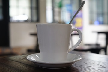 Coffee in a white cup with a saucer and spoon. Photo of a cup of coffee with a blur background on a wooden table in a cafe