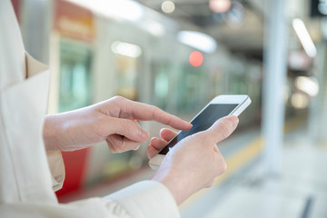 駅のホームでスマートフォンを触る女性の手元