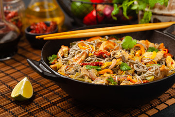Wheat noodles with black sesame, fried in a wok with chicken and vegetables. Front view.