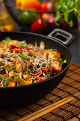Wheat noodles with black sesame, fried in a wok with chicken and vegetables. Front view.