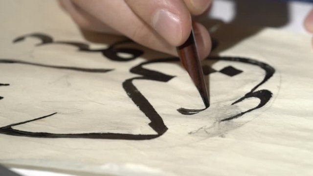 calligrapher writes arabic lettering with calligraphy pen on parchment. macro shot of islamic calligraphy art. close up slider dolly shot in calligrapher workshop. hand made arabic calligraphy.