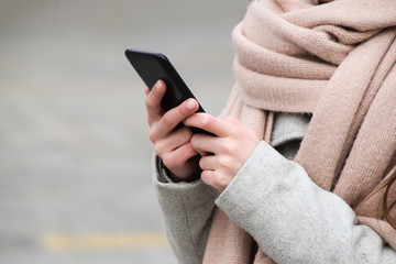 A woman on a cold day holds a cellphone in her hand on a street of a city - close up. Negative space.