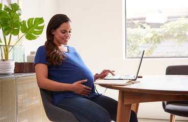 Pregnant Woman Using Laptop At Table Working From Home