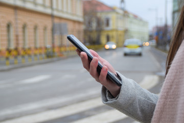 Woman's hand holds the phone waiting for a taxi.