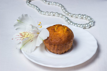 Cupcake and white flower on a white plate. Nearby lies white pearl jewelry