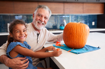 Portrait Of Grandfather And Granddaughter Carving Halloween Lantern From Pumpkin At Home