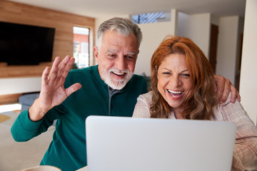 Senior Hispanic Couple At Home With Laptop Having Video Chat With Family