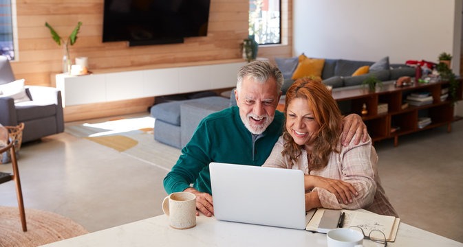Senior Hispanic Couple At Home Sitting At Table Using Laptop Together