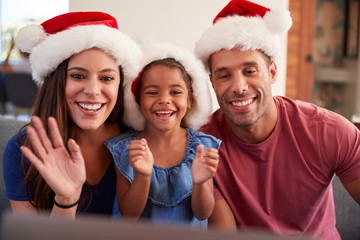 Hispanic Family Wearing Santa Hats With Laptop Having Video Chat At Christmas