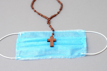 Closeup of medical mask and rosary with cross on gray background. Religion in medicine.