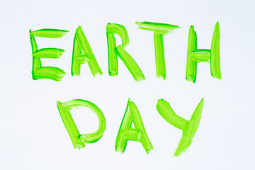 Top view of words Earth Day painted by green watercolor on white sheet of paper.