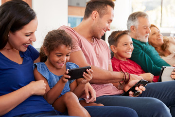 Multi-Generation Family On Sofa Watching TV And Playing With Digital Tablet And Mobile Phones