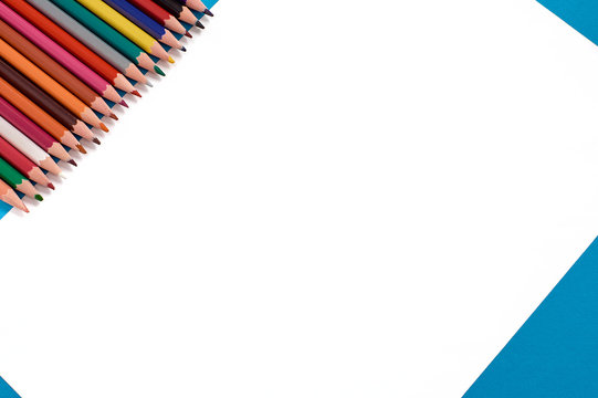 Colored pencils in a row. White sheet of paper on a blue background. Copy space