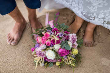 feet of the bride and groom on the beach with a wedding bouquet