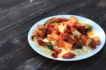 Couscous with chicken meat and vegetables, wooden brown background