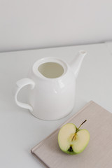 
half green apple and a white ceramic teapot on the table
