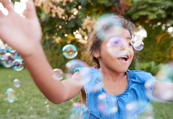 Young Hispanic Girl Chasing And Catching Bubbles In Garden