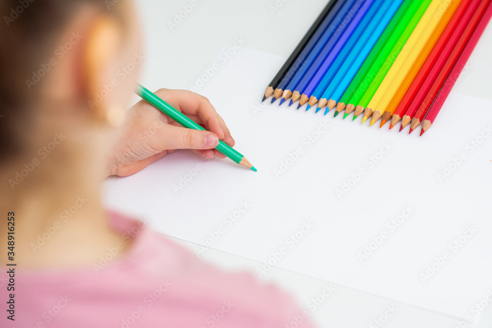 Wall mural Little girl is drawing on white paper using color pencil. Copy space for text. Mockup. Selective focus.