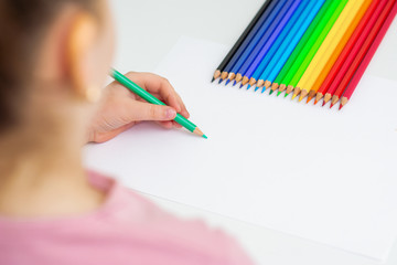 Little girl is drawing on white paper using color pencil. Copy space for text. Mockup. Selective focus.