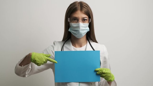 Female doctor in a mask of Caucasian appearance holds in her hands a4 blue sheet