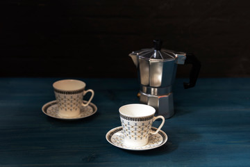 Cups and saucers for coffee and a geyser coffee maker on a blue wooden table