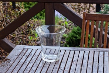 one large glass empty vase stands on a brown wooden table on the veranda in the street