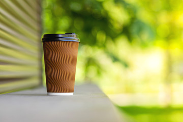 A paper cup of coffee on a wooden bar counter on the street.