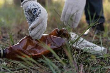 close-up hand of a man in gloves made of cloth raises a plastic bottle from the ground in the park.