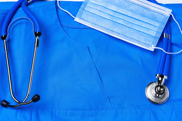 Doctor medical uniform with stethoscope and face mask on white wooden background close up