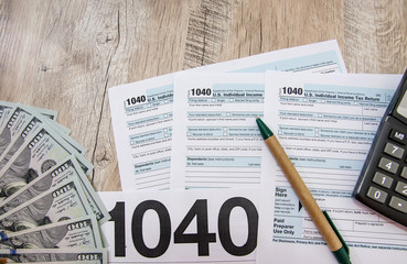 tax forms 1040 with calculator, pen and dollars on a wooden table