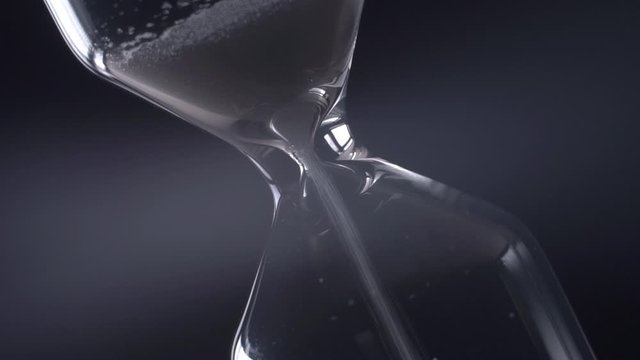 Rotating hourglass close-up on a black background. Time concept.
