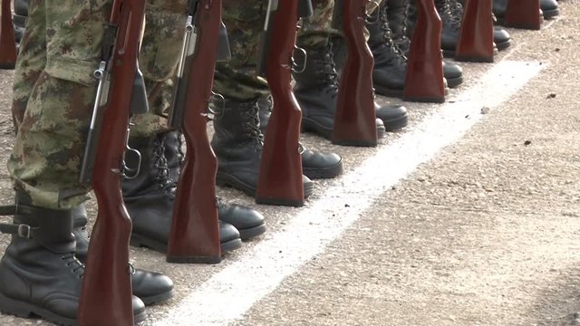 Soldiers in camouflage uniform standing at attention with guns at their feet.