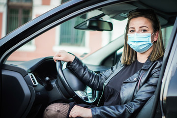 Young woman driving car with protective mask on her face. 