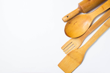 Four wooden cutlery lie in a row on the right side of the photograph on a white background. Wooden spoon, wooden fork. Wooden spatula and rolling pin