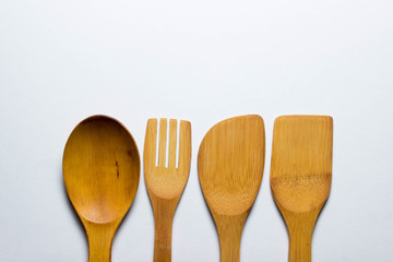 Four wooden cutlery lie in a row on a white background. Wooden spoon, wooden fork. And two wooden spatulas