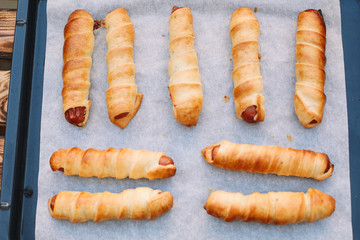Baked sausage rolls on the baking sheet on the wooden table. Hot dogs. Sausage in the dough.