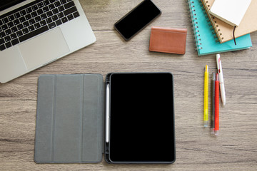 A top view of a business desk with tablet includes color pens, notebook, business card bag, computer laptop and smartphone on a wooden table to connect with others in the digital technology world. 