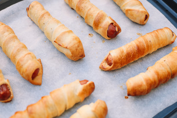 Baked sausage rolls on the baking sheet on the wooden table. Hot dogs. Sausage in the dough.