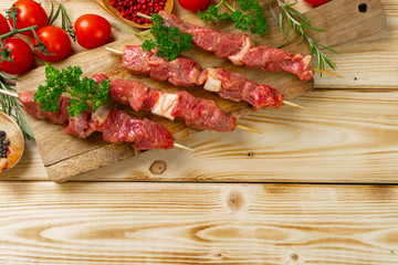 Raw kebab from meat on a wooden background with vegetables.