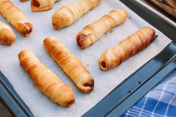 Baked sausage rolls on the baking sheet on the wooden table. Hot dogs. Sausage in the dough.