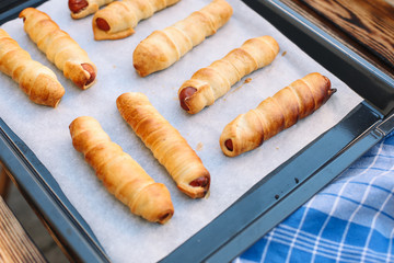Baked sausage rolls on the baking sheet on the wooden table. Hot dogs. Sausage in the dough.