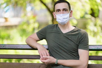 Young man in a medical mask sits in the park. Green background