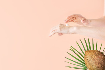 Young Caucasian woman rubbing in hands pure organic coconut oil on pink background with green palm leaf. Body skin care natural ingredients organic cosmetics concept