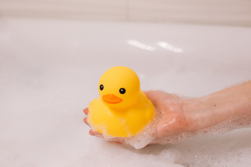 Girl is holding yellow rubber duck in the bath with bubble foam